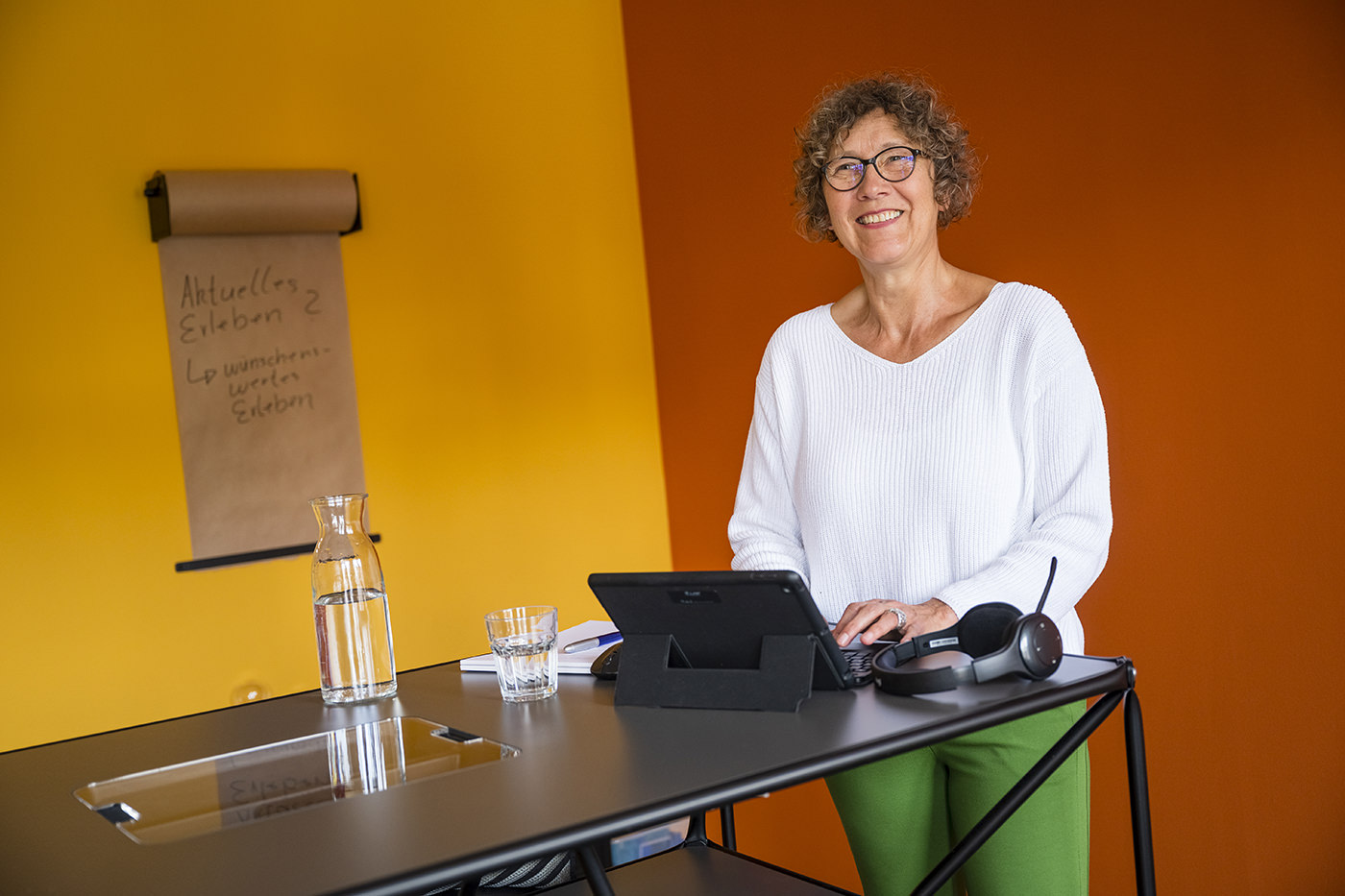 Das Digitalfoto zeigt eine lächelnde Frau am Steharbeitsplatz in farbigen Büro.